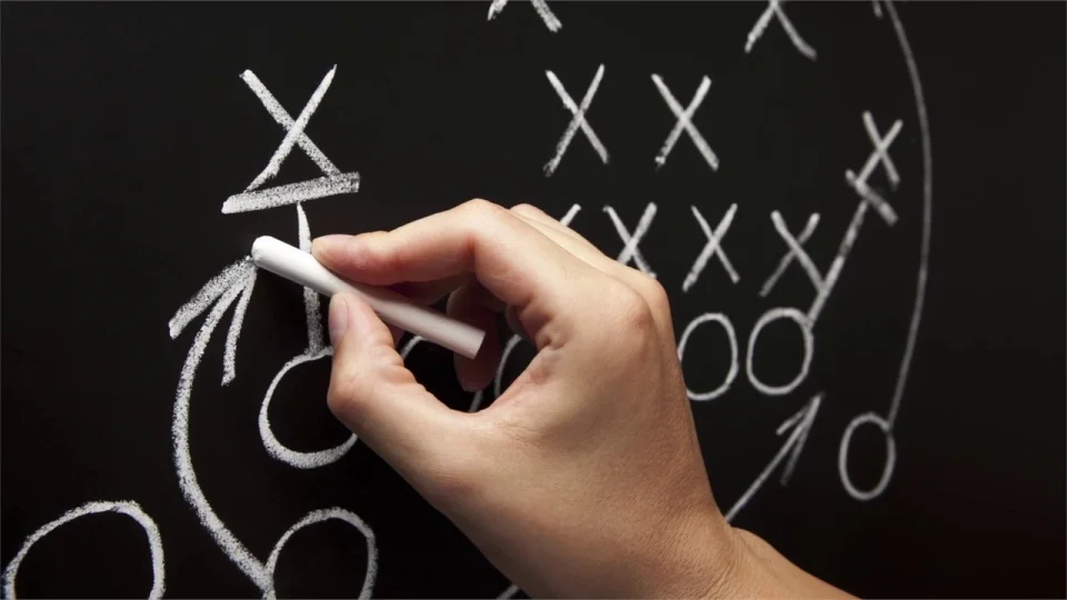 A person writing a football play on a chalkboard.